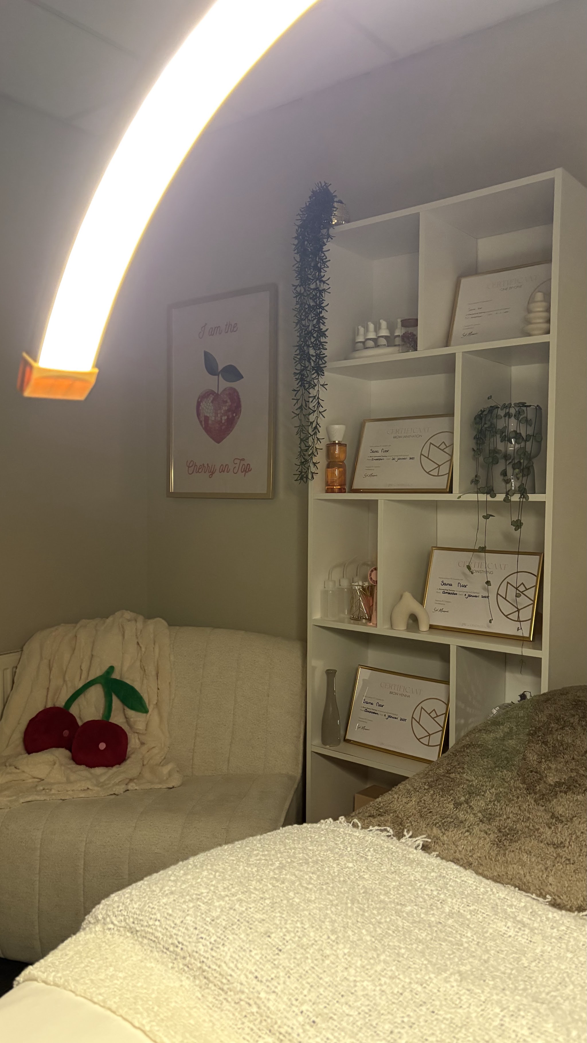 De salon van Goldn Atelier: behandelstoel, bank en wandkast onder een gouden booglamp